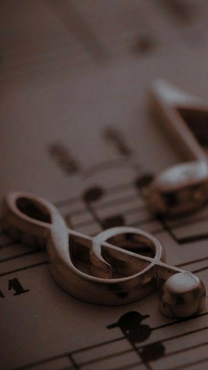 Close-up of a metallic treble clef pendant resting on a sheet of music.